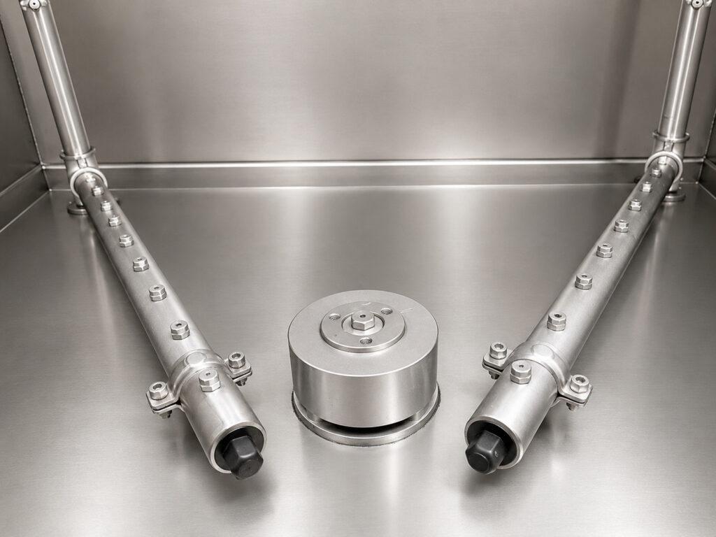Close-up of the underside sprayers and rotating drive assembly on a Winona Van Norman Stainless Steel Washer providing complete cleaning coverage beneath engine components.