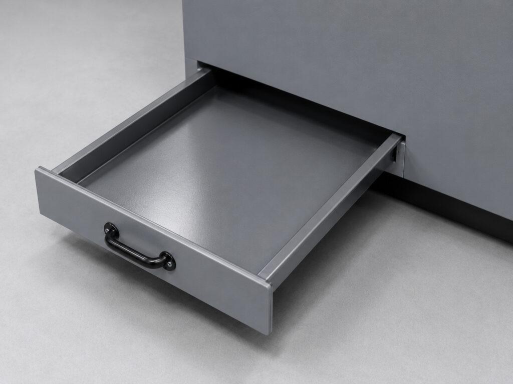 Close-up of the excess collection tray on a Winona Van Norman Grinding Bench used to capture grinding debris and spent material.