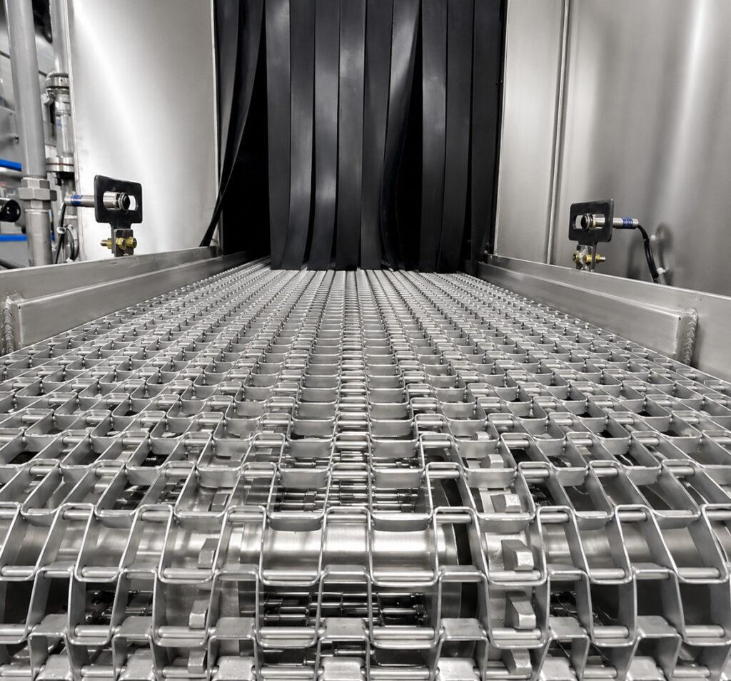 Close-up of the conveyor handling system on a Winona Van Norman Flow Through Washer transporting engine components through the cleaning process.