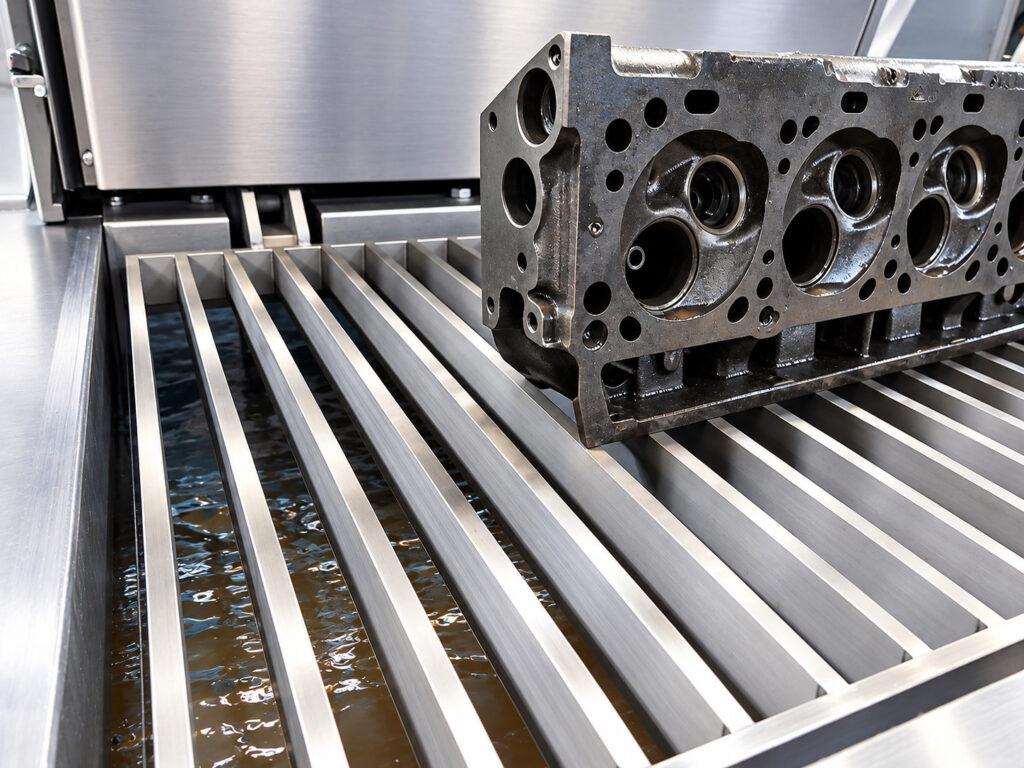 Engine cylinder head positioned inside a Winona Van Norman PAX Agitation Washer for thorough removal of oil, grease, carbon, and other contaminants during engine component cleaning.